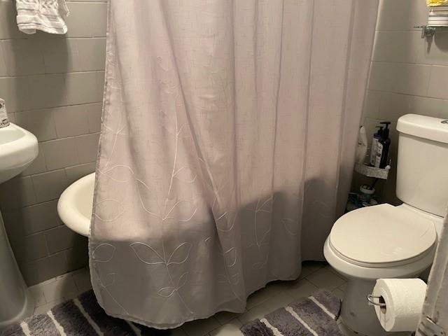 bathroom featuring tile patterned flooring, toilet, and tile walls