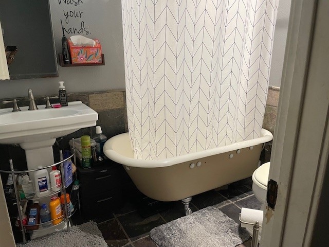 bathroom featuring a bathing tub, toilet, and tile walls