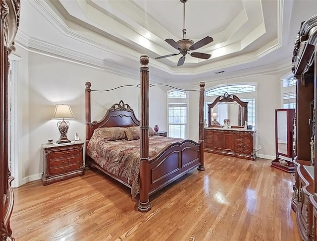 bedroom with ceiling fan, a raised ceiling, multiple windows, and light wood-type flooring