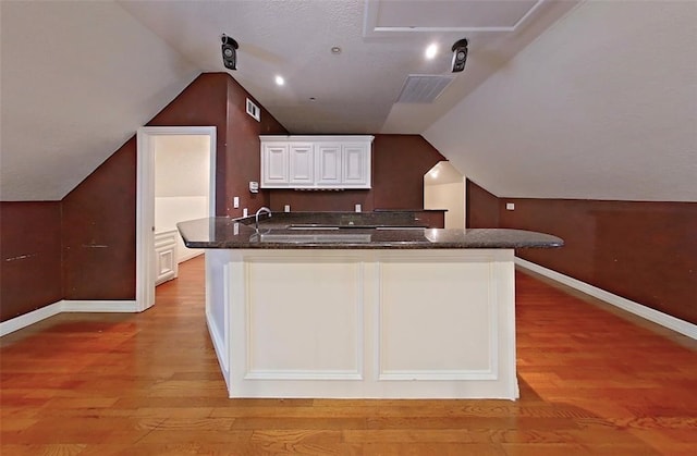 kitchen with dark stone counters, vaulted ceiling, light hardwood / wood-style floors, and white cabinetry