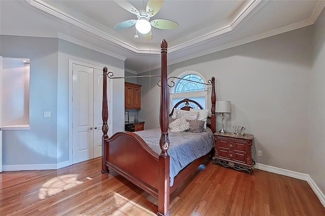 bedroom with ornamental molding, wood-type flooring, ceiling fan, and a tray ceiling