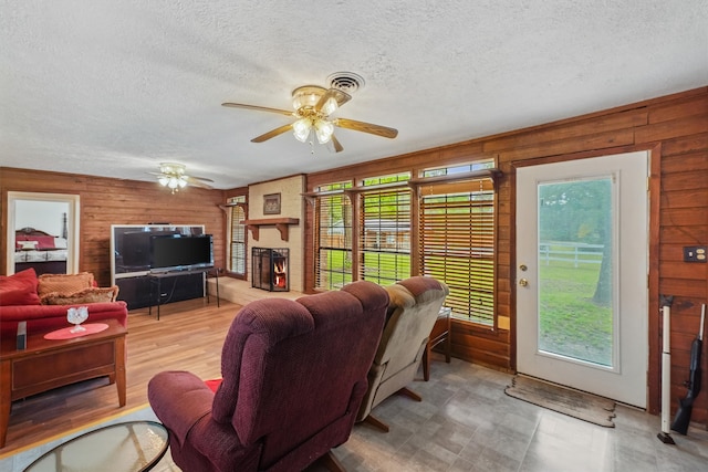 living room with a fireplace, a textured ceiling, ceiling fan, and wood walls