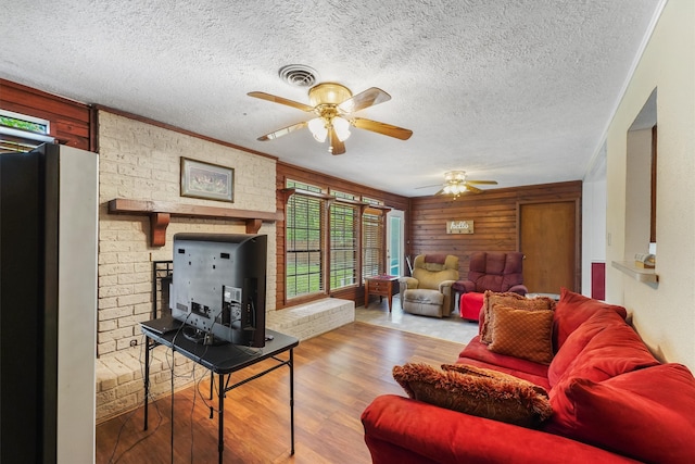 living room with ornamental molding, a textured ceiling, ceiling fan, hardwood / wood-style floors, and wood walls