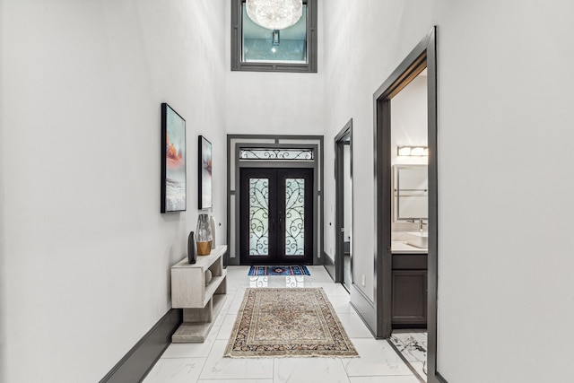 foyer entrance featuring a towering ceiling, marble finish floor, baseboards, and french doors