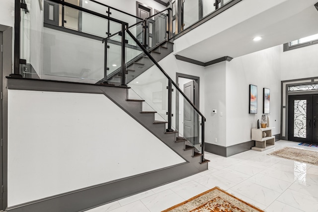 foyer featuring stairway, marble finish floor, a towering ceiling, and baseboards