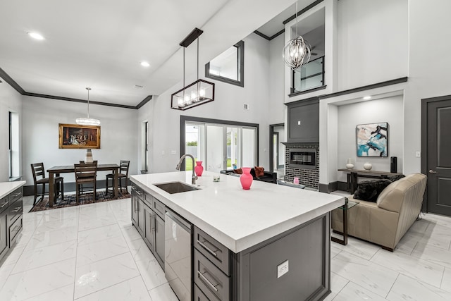 kitchen with an island with sink, a sink, light countertops, pendant lighting, and stainless steel dishwasher