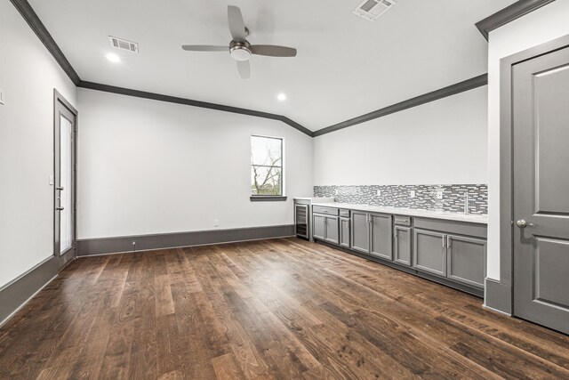 empty room featuring ornamental molding, lofted ceiling, visible vents, and dark wood finished floors