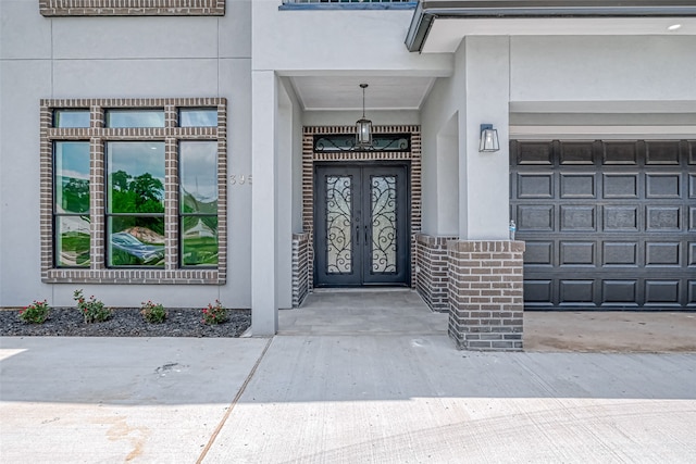 property entrance with french doors, brick siding, stucco siding, concrete driveway, and a garage