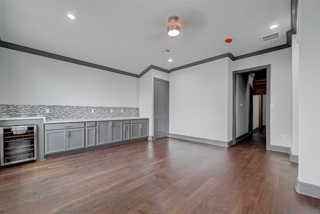 empty room featuring wine cooler, dark wood-style flooring, visible vents, ornamental molding, and baseboards