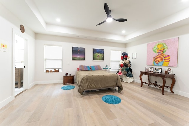 bedroom with light hardwood / wood-style floors, ceiling fan, and a tray ceiling