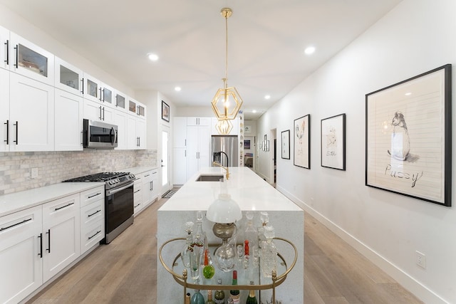 kitchen featuring white cabinets, appliances with stainless steel finishes, light hardwood / wood-style flooring, and a kitchen island with sink