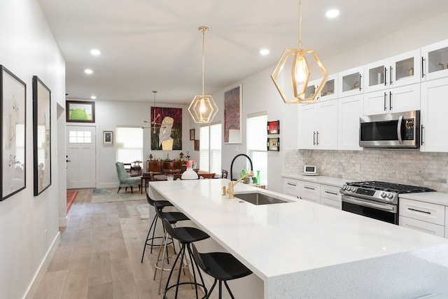 kitchen with hanging light fixtures, white cabinets, backsplash, appliances with stainless steel finishes, and light hardwood / wood-style floors