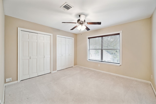 unfurnished bedroom featuring light colored carpet, multiple closets, and ceiling fan