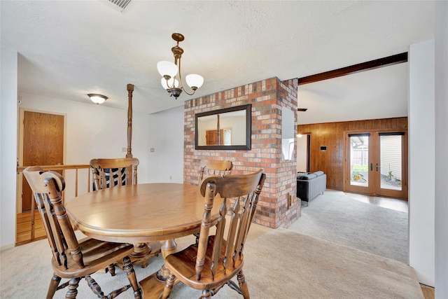 dining space with a chandelier, a textured ceiling, light carpet, and wood walls