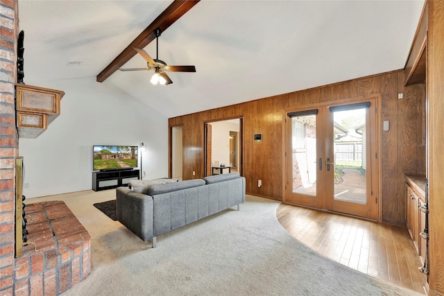 carpeted living room with french doors, wooden walls, and lofted ceiling with beams