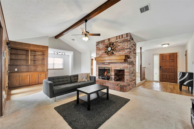 carpeted living room with a brick fireplace, lofted ceiling with beams, a textured ceiling, and ceiling fan