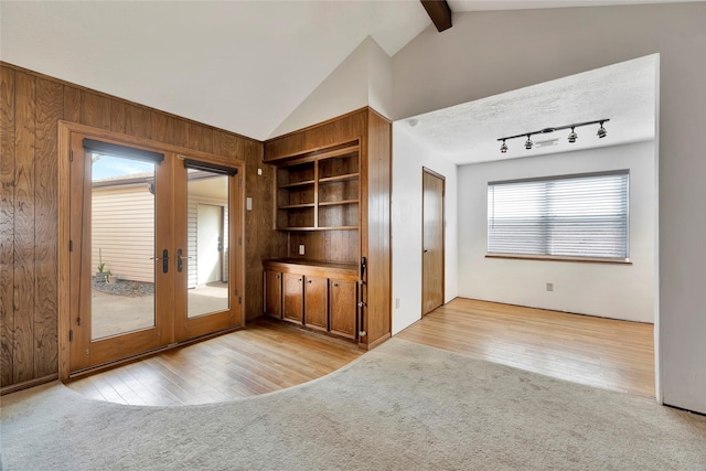 interior space with vaulted ceiling with beams, built in shelves, wooden walls, and french doors