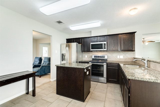 kitchen featuring sink, a center island, stainless steel appliances, tasteful backsplash, and light stone counters