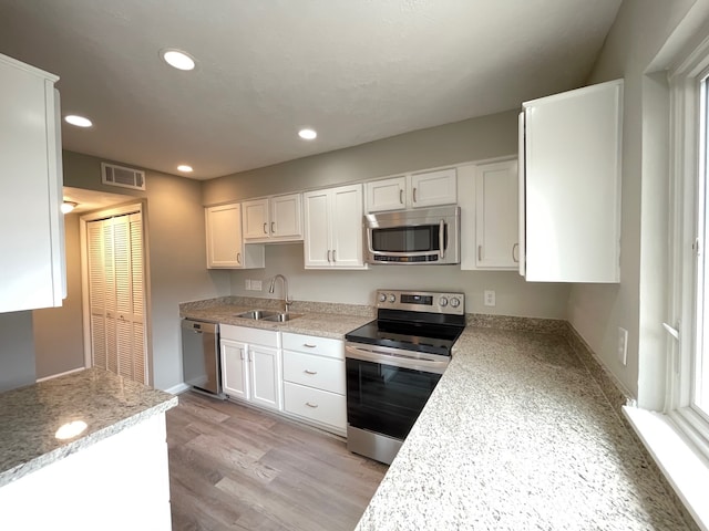 kitchen with appliances with stainless steel finishes, white cabinetry, sink, and light wood-type flooring