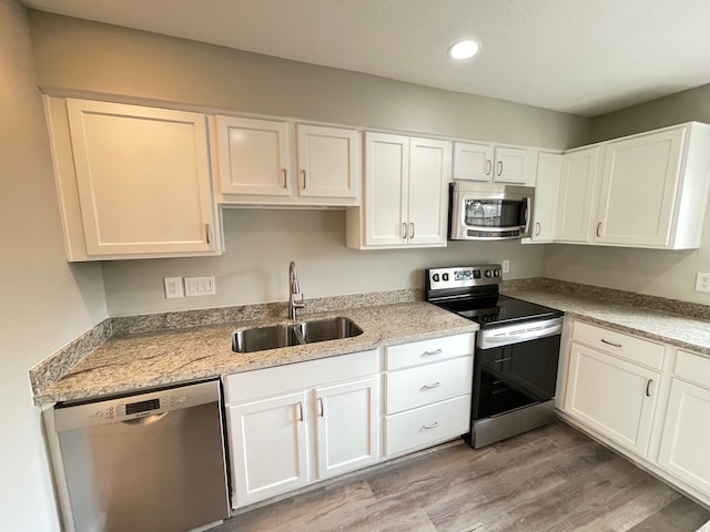 kitchen with appliances with stainless steel finishes, white cabinets, light hardwood / wood-style flooring, light stone countertops, and sink