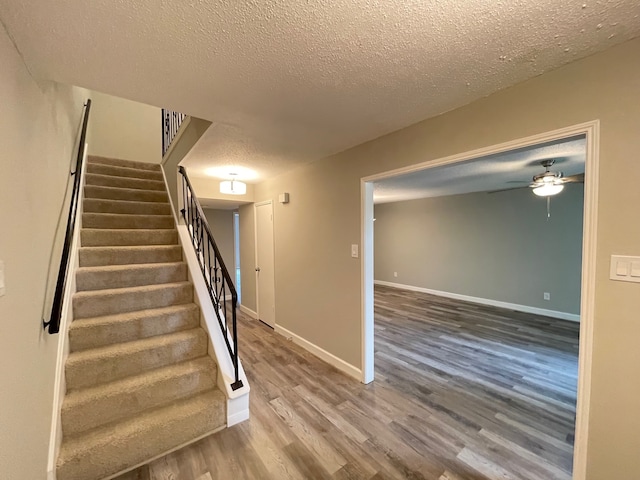 stairs with ceiling fan, a textured ceiling, and dark wood-type flooring