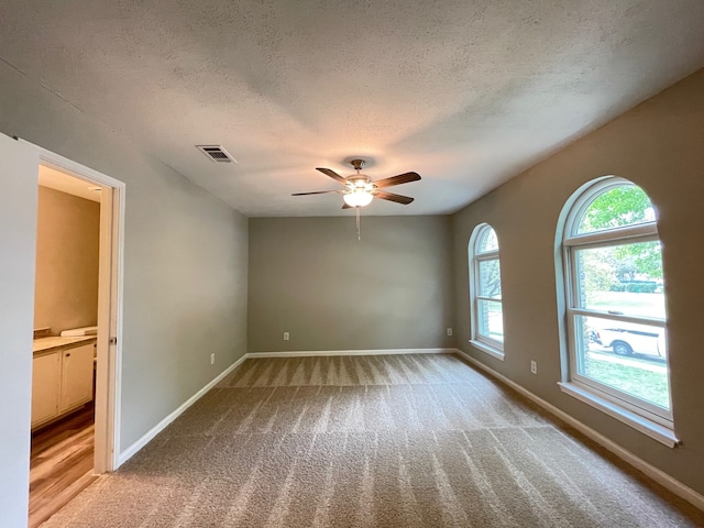 empty room with light hardwood / wood-style flooring, a healthy amount of sunlight, ceiling fan, and a textured ceiling