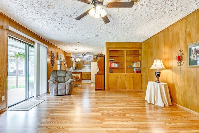 living room featuring built in shelves, a textured ceiling, ceiling fan, light hardwood / wood-style floors, and wood walls