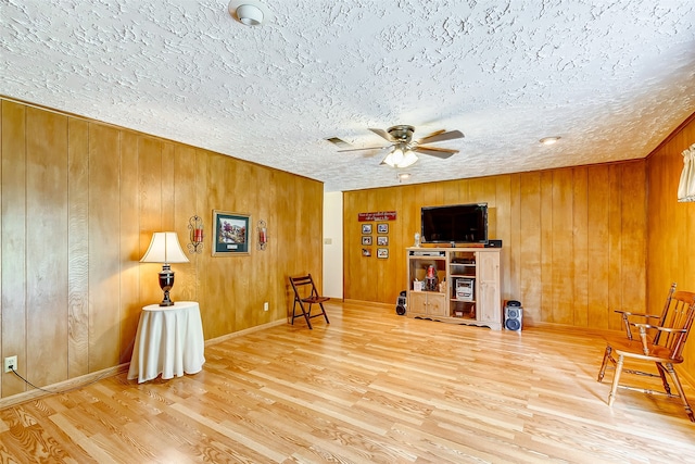 sitting room with hardwood / wood-style floors, a textured ceiling, ceiling fan, and wood walls