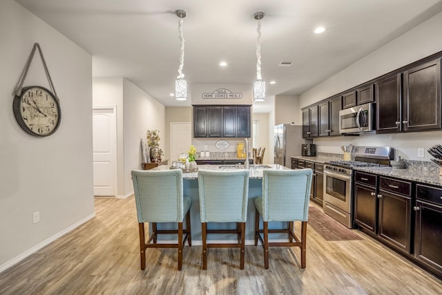 kitchen featuring appliances with stainless steel finishes, dark brown cabinets, a kitchen island with sink, and a breakfast bar area