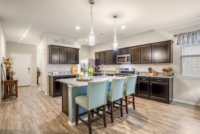 kitchen with stainless steel appliances, a kitchen breakfast bar, pendant lighting, a center island with sink, and dark brown cabinets