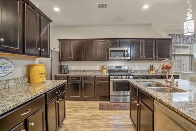 kitchen with dark brown cabinetry, stainless steel appliances, sink, light hardwood / wood-style flooring, and hanging light fixtures