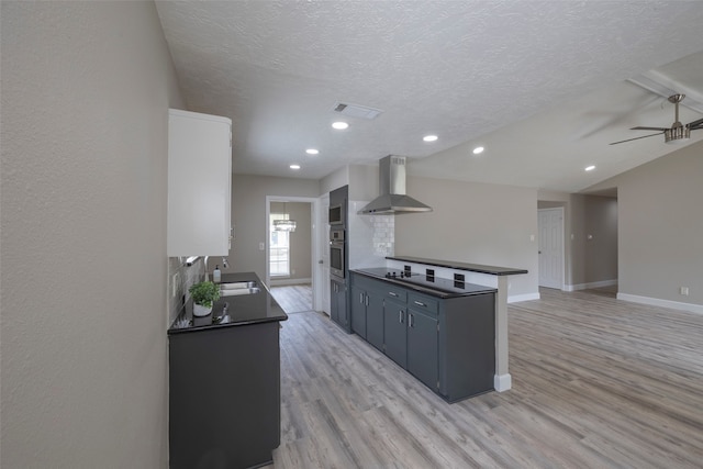 kitchen featuring stainless steel oven, sink, wall chimney exhaust hood, light hardwood / wood-style floors, and ceiling fan