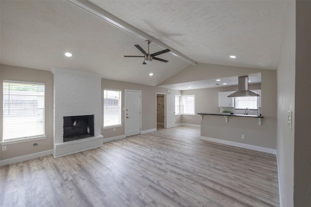 unfurnished living room featuring light wood finished floors, a brick fireplace, lofted ceiling with beams, and baseboards