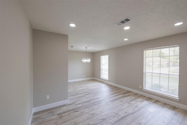 empty room featuring visible vents, baseboards, light wood-style floors, and a textured ceiling