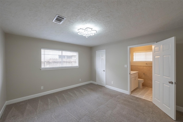 unfurnished bedroom with visible vents, connected bathroom, baseboards, light colored carpet, and a textured ceiling