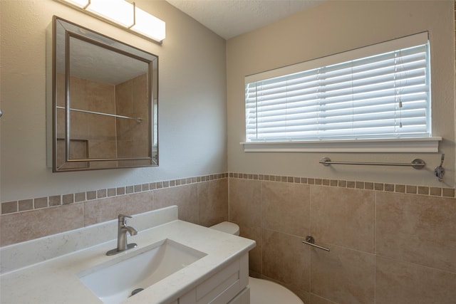 bathroom with toilet, tile walls, vanity, and a textured ceiling