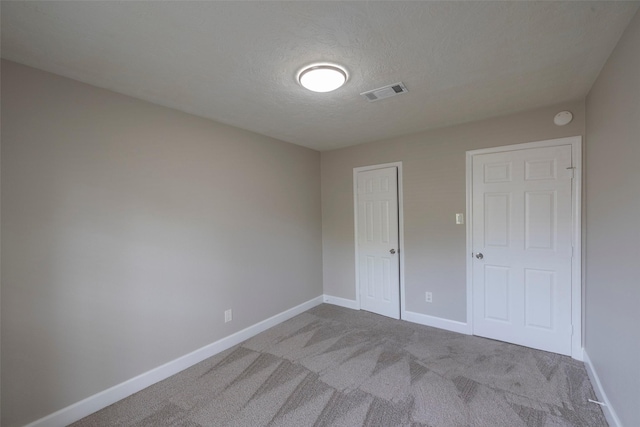 carpeted empty room featuring visible vents, a textured ceiling, and baseboards