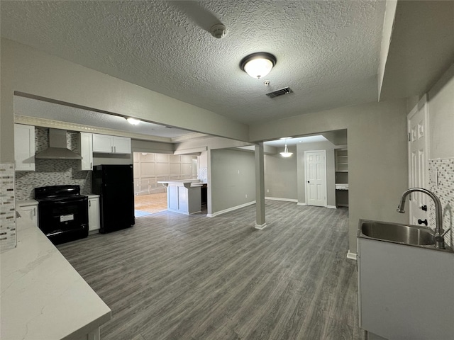 kitchen featuring tasteful backsplash, wall chimney exhaust hood, black appliances, white cabinetry, and sink