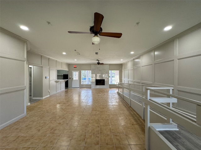 interior space with white cabinets, light tile floors, a large fireplace, and ceiling fan