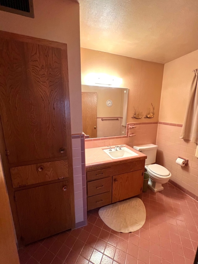 bathroom with oversized vanity, toilet, a textured ceiling, tile walls, and tile floors