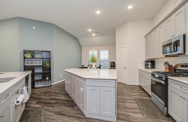 kitchen with lofted ceiling, dark hardwood / wood-style floors, stainless steel appliances, a center island, and tasteful backsplash