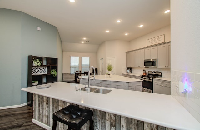 kitchen featuring a center island with sink, stainless steel appliances, dark wood-type flooring, and gray cabinets