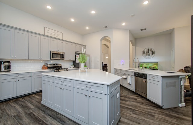 kitchen with stainless steel appliances, kitchen peninsula, gray cabinets, dark wood-type flooring, and sink