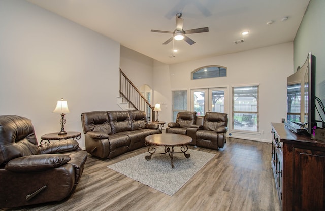 living room with a towering ceiling, light hardwood / wood-style floors, ceiling fan, and french doors