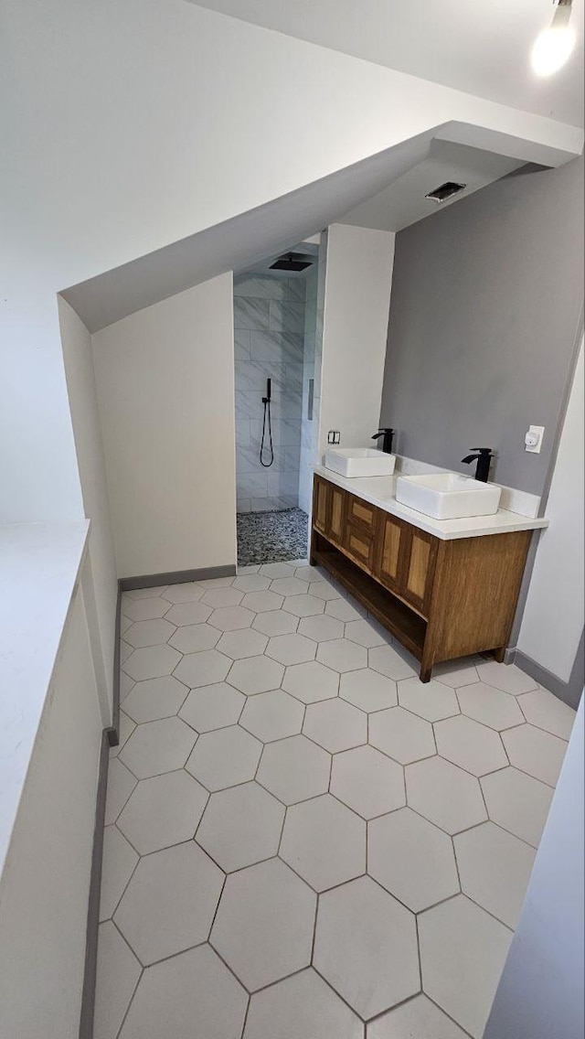 bathroom with a tile shower, vanity, and vaulted ceiling