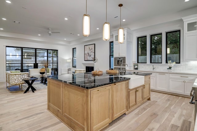 kitchen featuring an island with sink, sink, light hardwood / wood-style flooring, decorative light fixtures, and decorative backsplash