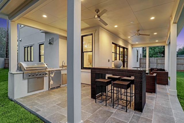 view of patio featuring ceiling fan, grilling area, an outdoor bar, and exterior kitchen