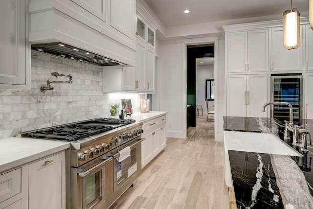 kitchen with light stone counters, white cabinets, custom range hood, double oven range, and light hardwood / wood-style floors