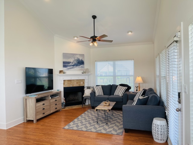 living room with ceiling fan, crown molding, a tiled fireplace, and light hardwood / wood-style floors