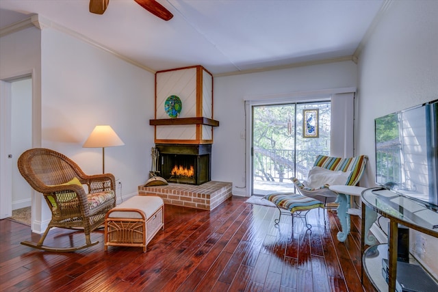 sitting room with dark hardwood / wood-style floors, a brick fireplace, ornamental molding, and ceiling fan